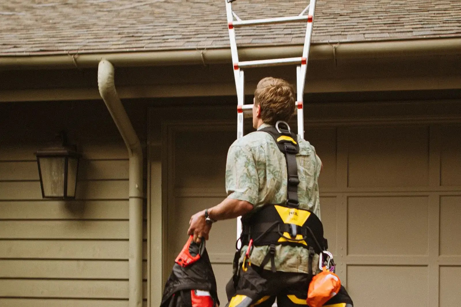 Roofer with a tool belt climbing a ladder past a gutter