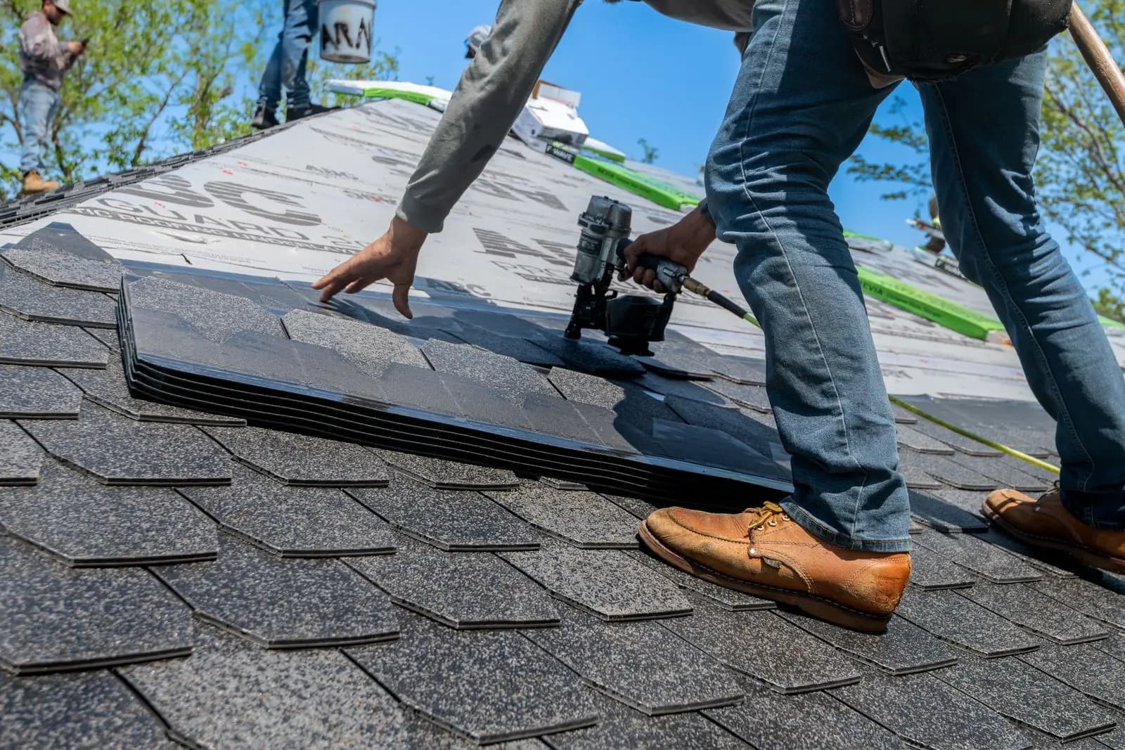 Roofer nailing architectural asphalt shingles with a nail gun