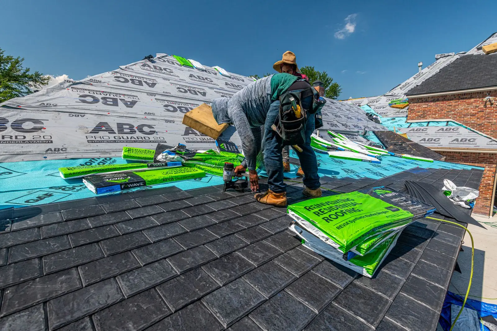 Roofers stacking bundles of shingles on a roof under synthetic underlayment